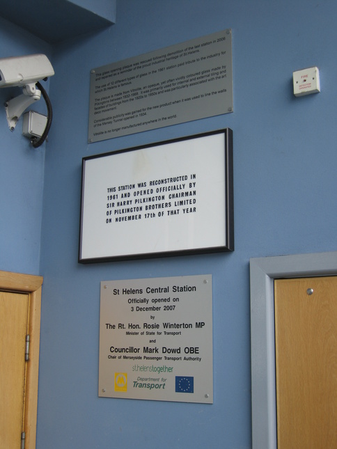 This glass opening plaque was
rescued following demolition of the last station in 2006 and repaired
as a reminder of the proud industrial heritage of St Helens.  The use
of 12 different types of glass in the 1961 station paid tribute to the
industry for which St Helens is famous.  The plaque is made from
Vitrolite, an opauq, yet often vividly coloured glass made by
Pilkingtons between 1932-1968.  It was primarily used for internal and
external tiling and facades of buildings from the 1920s to 1950s and
was particularly associated with the art deco movement.  Considerable
publicity was gained for the new product when it was used to line the
walls of the Mersey Tunnel opened in 1934.  Vitrolite is no longer
manufactured anywhere in the world.  /  THIS STATION WAS RECONSTRUCTED
IN 1961 AND OPENED OFFICIALLY BY SIR HARRY PILKINGTON CHAIRMAN OF
PILKINGTON BROTHERS LIMITED ON NOVEMBER 17th OF THAT YEAR  /  St
Helens Central Station Officially opened on 3 December 2007 by The
Rt. Hon Rosie Winterton MP Minister of State for Transport and
Councillor Mark Dowd OBE Chair of Merseyside Passenger Transport
Authority.